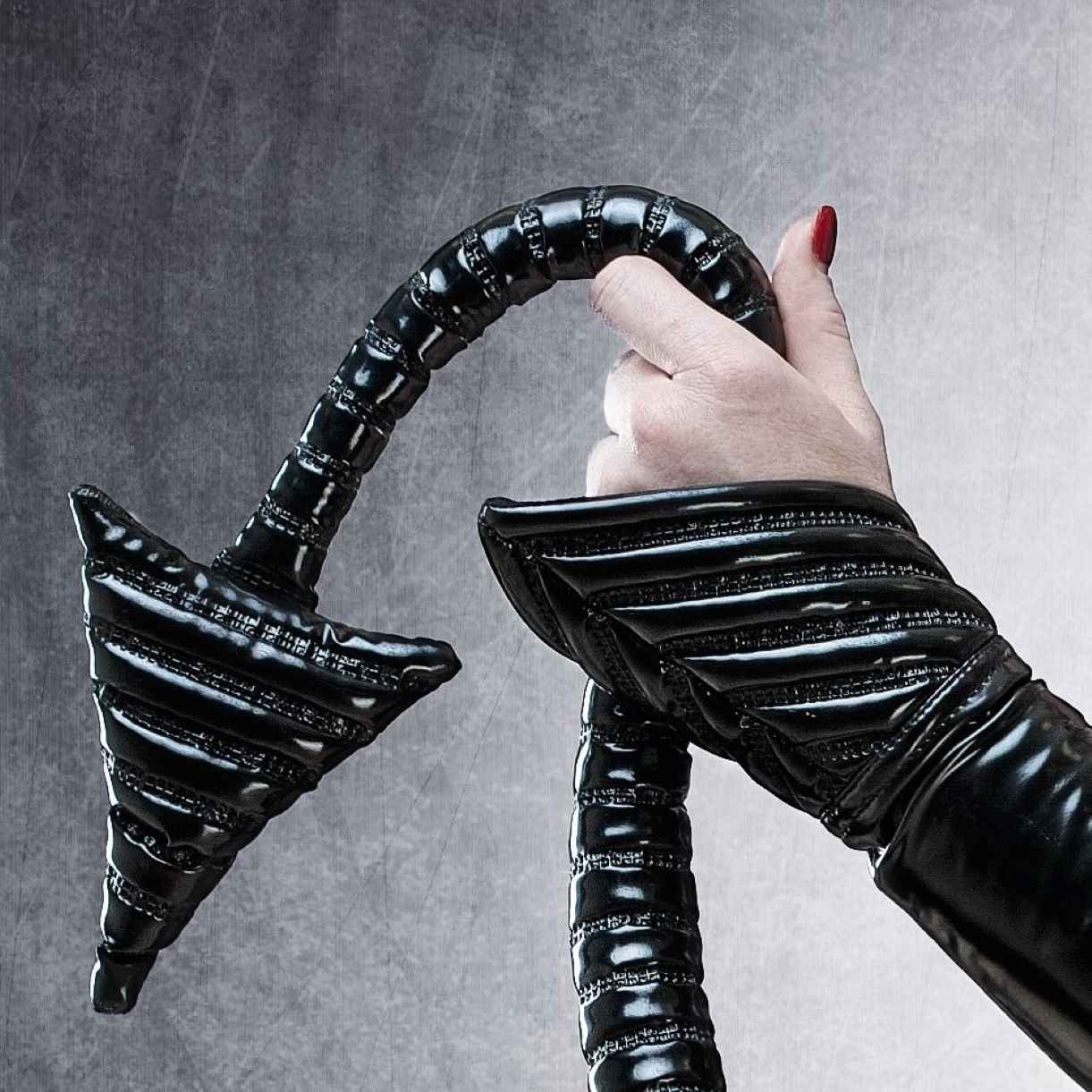 Tail DK – glossy black PVC tail with metal buckle details and ribbed segmentation, close-up