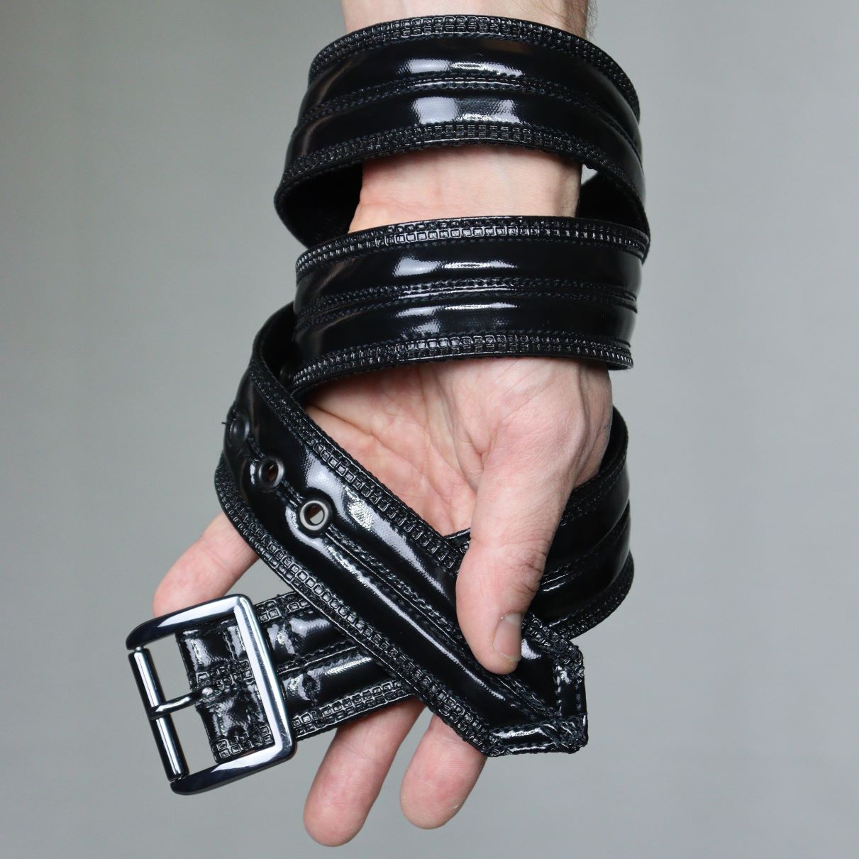 Gun Metal Belt – glossy black PVC with silver-tone hardware and adjustable buckle, hand detail view